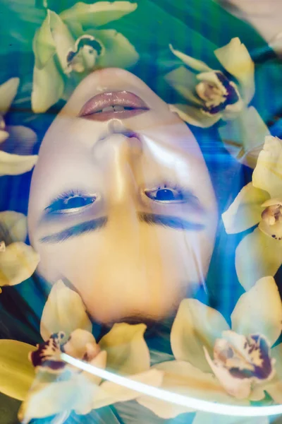 Retrato de una hermosa chica con maquillaje y flores de orquídea alrededor de su cara. Mujer y flores. Primavera . — Foto de Stock
