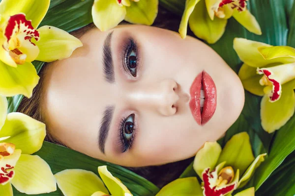 Portrait of beautiful girl with make-up and orchid flowers around her face. Woman and flowers. Spring.