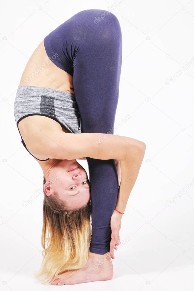 Young woman practicing yoga, standing in an exercise leaning forward to straight legs, uttanasana pose, balance workout, sportswear, pants, bra, short t-shirt, studio room light white background