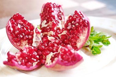 Parçalara ayrılmış kırmızı bir nar, nane filizi ile süslenmiş beyaz bir tabakta yatıyor..