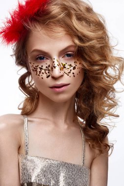 Hafif bir makyaj ile altın elbiseli güzel kız. Onun baş ve bukleler kırmızı tüyler ile model. Tatil fotoğraf. 