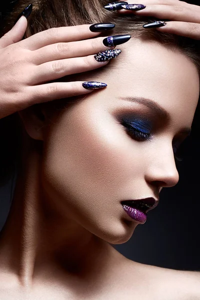 Young woman with creative make-up and violet lips with a gradient and sparkles on the face. Beautiful model with bright nails with rhinestones.