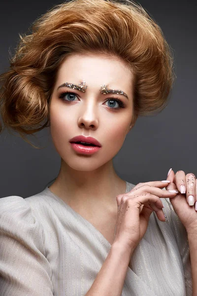 Young girl with lush hairstyle and make-up Nude. Beautiful model with sequins on the eyebrows and delicate pink manicure. — Stock Photo, Image