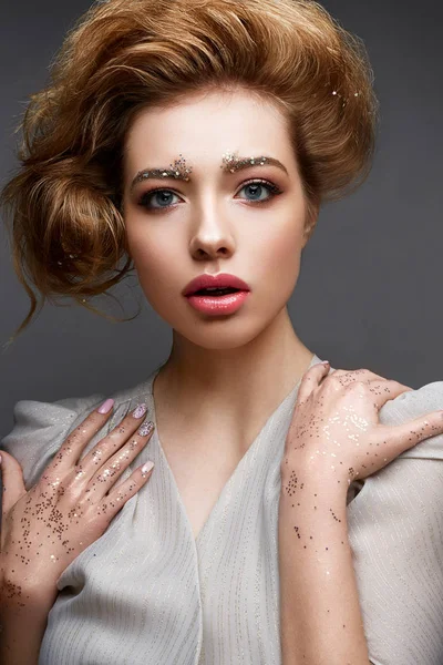 Young girl with lush hairstyle and make-up Nude. Beautiful model with sequins on the eyebrows and delicate pink manicure. — Stock Photo, Image