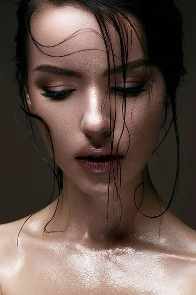 A young girl with shining wet skin and wet hair on her face. Beautiful model with creative bright makeup. Beauty of the face.
