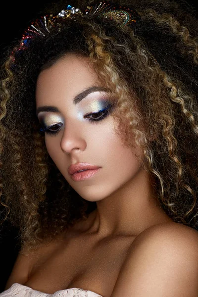 Una joven afroamericana con maquillaje creativo y rizos pequeños. Un hermoso modelo con la piel perfecta y una corona de piedras en la cabeza . — Foto de Stock