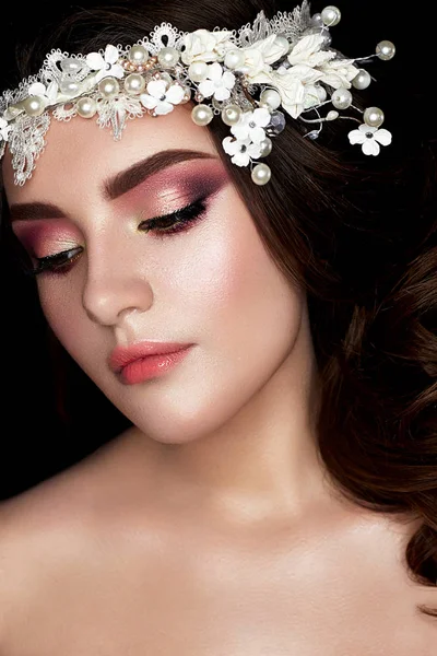 Une jeune fille à l'image d'une mariée avec une couronne florale sur la tête et des boucles. Un beau modèle avec un maquillage lumineux et une peau parfaite — Photo