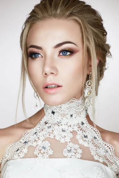 Une jeune fille à l'image d'une mariée dans une robe de mariée et de belles boucles d'oreilles brillantes. Un beau modèle avec un maquillage lumineux et une peau parfaite — Photo