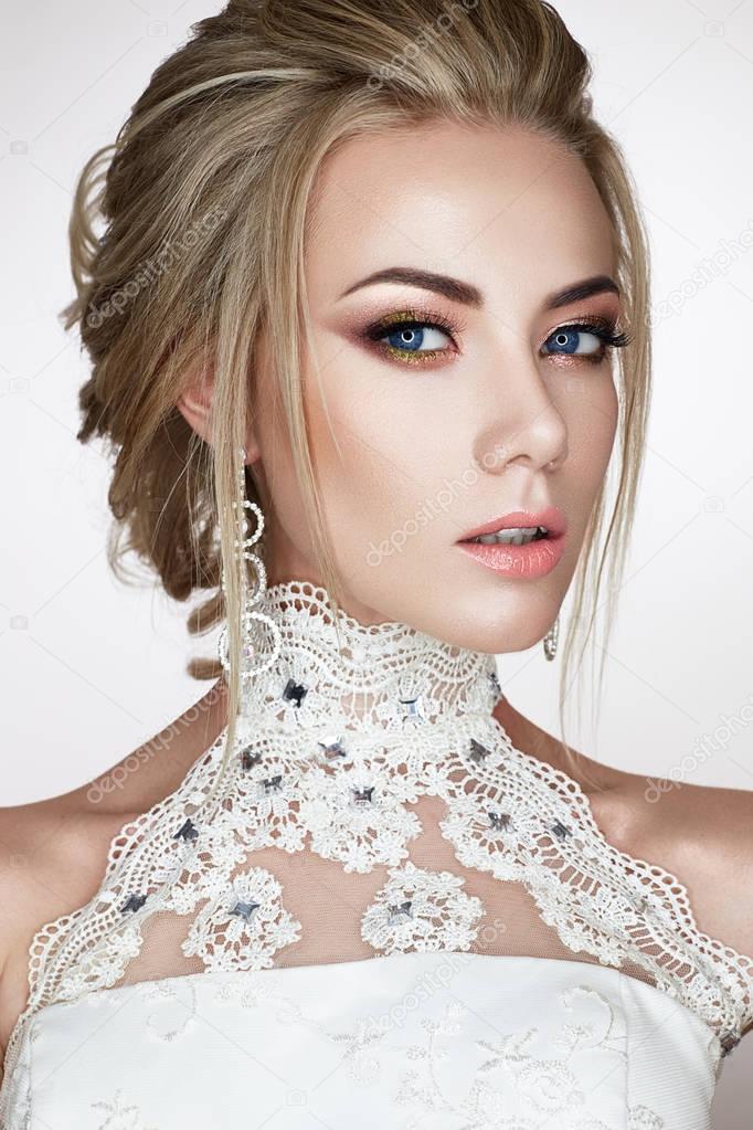A young girl in the image of a bride in a wedding dress and beautiful shiny earrings. A beautiful model with a bright makeup and perfect skin