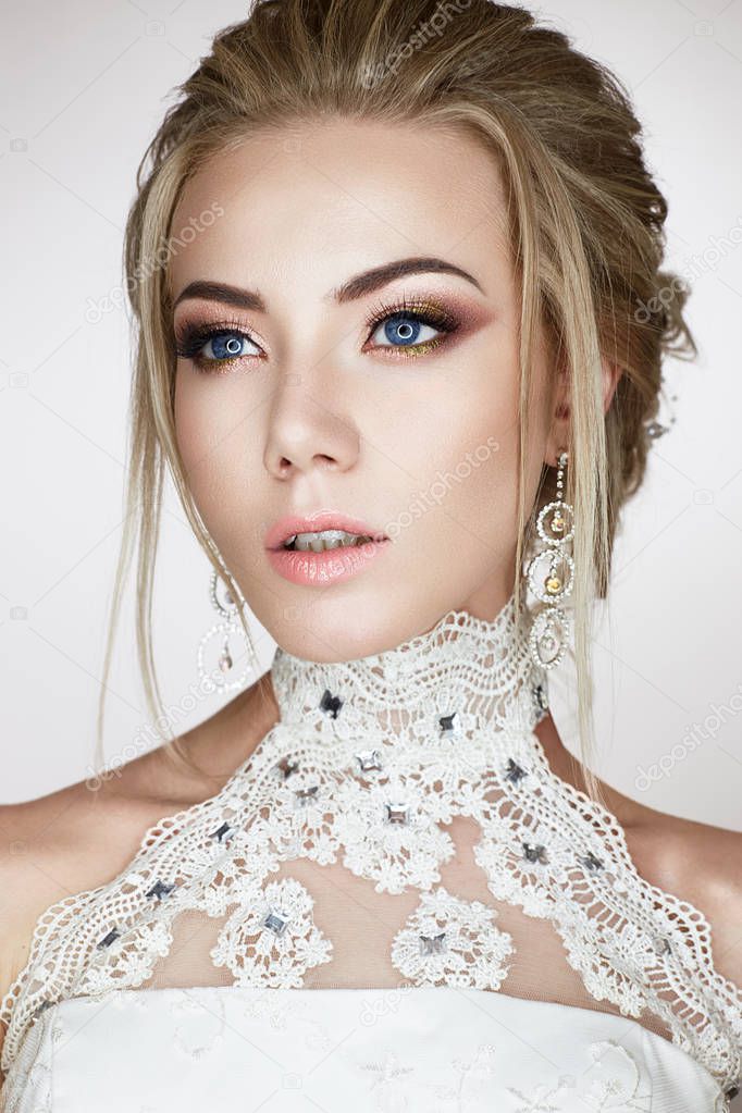 A young girl in the image of a bride in a wedding dress and beautiful shiny earrings. A beautiful model with a bright makeup and perfect skin