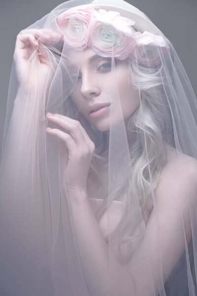 A young girl in the image of a bride with a veil on her face. Beautiful model with a wreath of flowers on her head