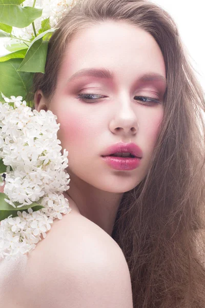 Une jeune fille au maquillage lilas et lumineux et créatif. Beau modèle avec des fleurs et des cheveux longs. Fond blanc isolé. Pure peau brillante. Beauté du visage — Photo