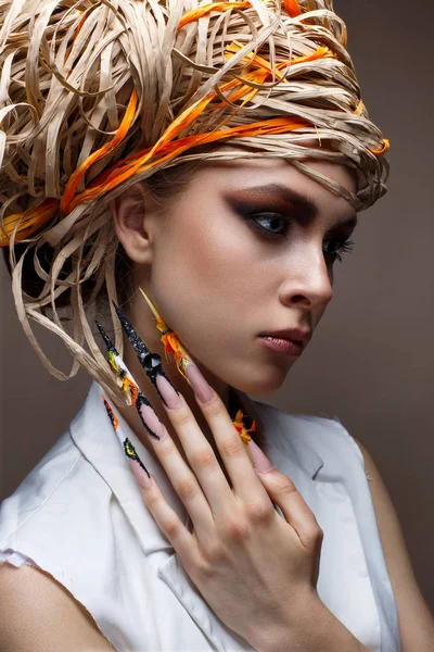 Una joven con uñas largas decoradas y maquillaje creativo brillante. Hermosa modelo con un sombrero de paja en la cabeza. Hermosa manicura. Piel brillante pura Imagen de archivo