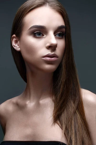 A young girl with straight flowing hair. A beautiful model with a gentle nude makeup and shining skin.