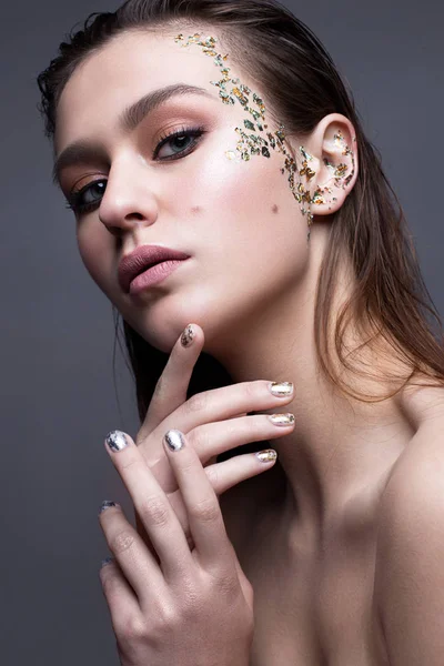 A young girl with a gentle classical make-up and loose hair. Beautiful model with creative art make-up and manicure from foil. Beauty of face and shining skin.