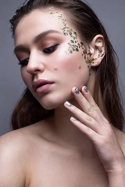 A young girl with a gentle classical make-up and loose hair. Beautiful model with creative art make-up and manicure from foil. Beauty of face and shining skin.