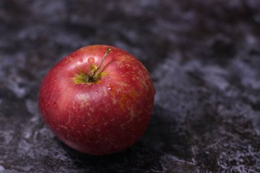 Koyu arkaplanda su damlaları olan kırmızı bir elma. 