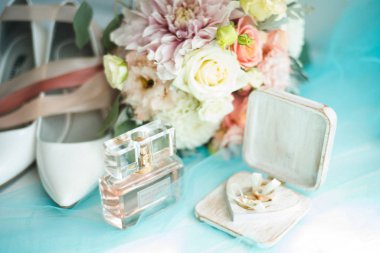 Güzel gelin sabahı bir buket çiçekle beyaz terlik parfümü Givenchy ve alyanslar bir kutuda