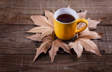 Sarı fincan çay ve yaprakları rustik ahşap arka plan üzerinde