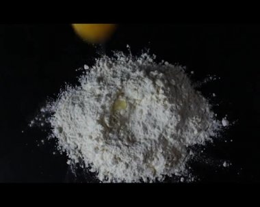 Yumurta siyah arka planda unun içine düşer. Evde yemek pişirme kavramı. Hamur yoğuruyorum. Karantinada ev yapımı yemek. Yatay yönelim