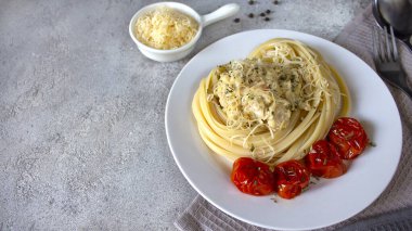 İçinde hindi ve beyaz tabakta peynir serpiştirilmiş domatesli makarna. Havlunun üstünde bir tabak, spagetti için çatal ve kaşığın yanında. Uzayı kopyala Reklam afişi. Yatay yönelim