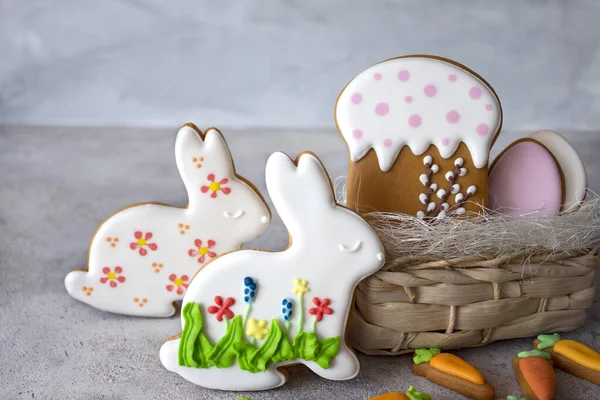 Easter cakes on a gray background and a wicker basket. Gingerbread in the form of a hare, carrot, egg and cake. Copy space. The concept of the Easter holiday and handmade. Banner, layout