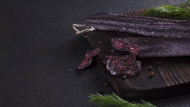 Sajuk sade sosisin koyu pankartı. Ahşap bir tahtanın üzerinde kurutulmuş sosis ve karabiber. Basturma. Kötü ruh hali. Yaratıcı ve lezzetli servis. Alçakgönüllülük. Boşluğu kopyala
