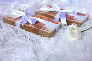 Beyaz bir kurdeleyle bağlanmış bir tomar para beyaz bir dantelin üzerinde yatıyor.