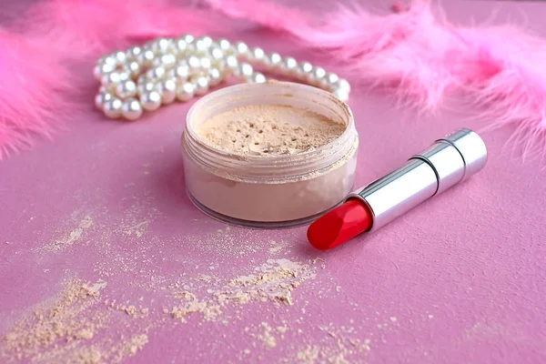 Loose make-up powder, light powder, white pearl necklace beads and boudoir in the dressing room pink retro lipstick in vintage style on a pink background and pink flamingo feathers