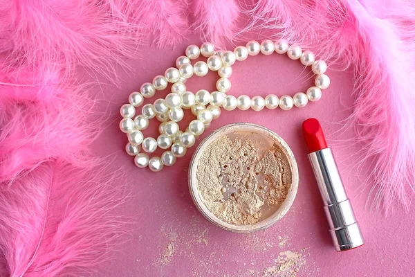 Loose make-up powder, light powder, white pearl necklace beads and boudoir in the dressing room pink retro lipstick in vintage style on a pink background and pink flamingo feathers