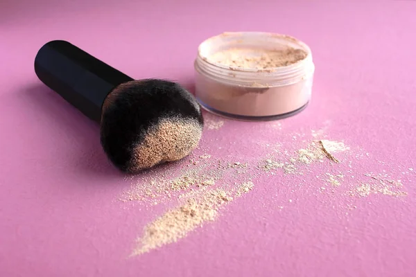 Loose compact mineral powder for face and fair skin shade ivory porcelain and a large brush for powder and visage on a pink background