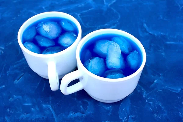 Blue royal color background and two white cups with blue water with ice cubes, a cooling drink