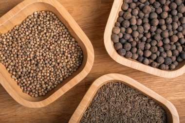 Cumin, coriander and pepper in bamboo jars on a wooden background.