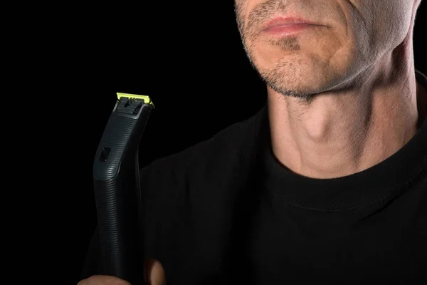 Muž si holí obličej elektrickým holicím strojem. Detailní záběr, černé pozadí. — Stock fotografie