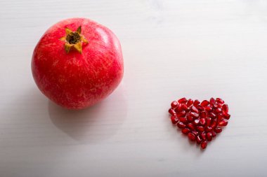 Pomegranate, fresh red seeds on white background. Heart shape.
