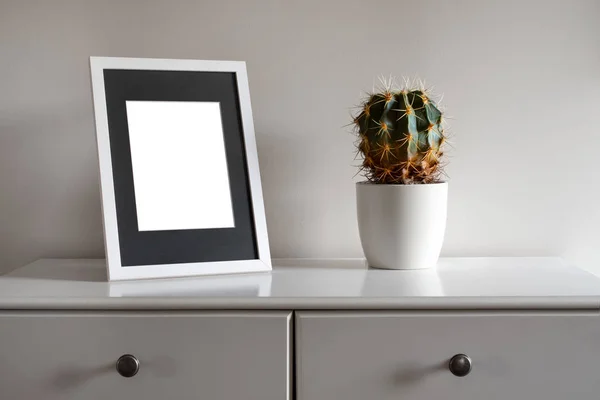 Maqueta de marco blanco con maceta en una cómoda blanca . — Foto de Stock