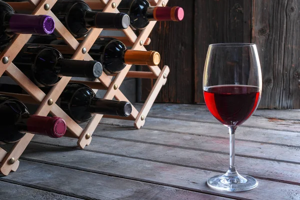 A glass of red wine and a wine rack with wine bottles on an old wooden cellar background
