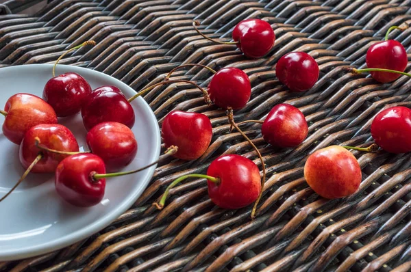 Cherries in the white dish and on the wicker backround — Stock Photo, Image