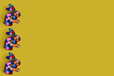 Tavşan şekilli zencefilli çörek ve sarı arka planda renkli toplar. Paskalya konsepti. Metin için yer.