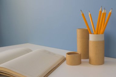 Sarı kalemli kağıt tüpler ve mavi arka planda defter. Evdeki kağıt tüplerin nasıl yeniden kullanılacağını gösteren geri dönüşüm konsepti. Boşluğu kopyala