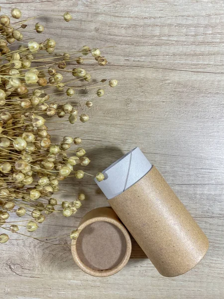 Paper tube with paper cover on wooden background with bouquet of dry flax. Flat lay recycle concept. Top view. Vertical mobile photo.