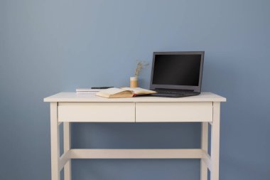 Beyaz masadaki siyah ekranlı laptop. Yaratıcı bir girişimcinin merkez ofisi. Mavi arka planlı minimalist modern yaratıcı çalışma alanı. Boşluğu kopyala.