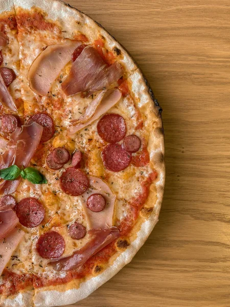 木製のテーブルの上に熱いイタリアのピザのトップビュー 揚げたてのフラットブレッドにサラミ チーズ 揚げハム 新鮮な緑のバジルをトッピング 縦型携帯写真 — ストック写真