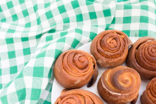 Close up of hot fresh homemade French buns cinnabones with cinnamon, tasty homemade dessert on white plate on wooden table with green tablecloth. Copyspace, selective focus — Stock Photo, Image