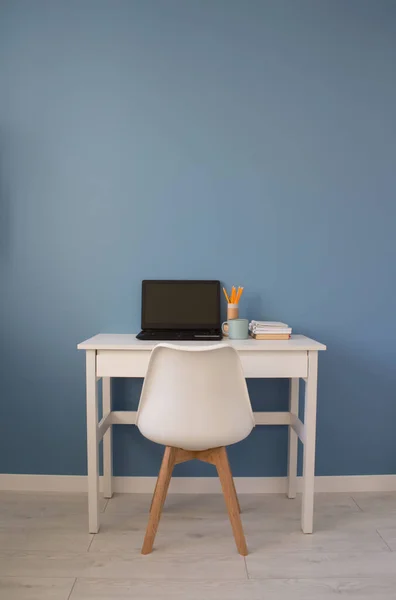 Empty home office of creative entrepreneur with black laptop on white table during lunch break. Modern workspace with blue cup of coffee and yellow pencils in reusable paper tube, vertical composition — Stock Photo, Image