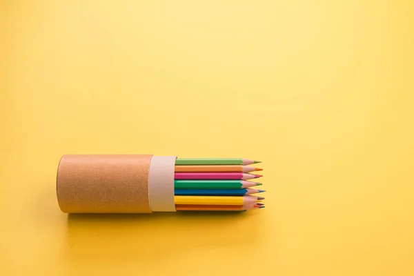 Color pencils in reusable paper tube packaging on bright yellow as creative background or mockup with copyspace. Back to school or reusable packaging concept