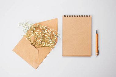 Güzel klasik düz kompozisyon, ahşap kalem, kraft kağıt defter ve kahverengi zarf, açık gri arka planda açık gri bebek nefesi çiçekleri, metin alanınız için kopya alanı.