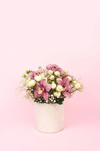 Beautiful bouquet of orchids, roses and gypsophila, Baby\'s-breath flowers in decorative paper tube packaging on pink background, copy space. Selective focus, celebrating or delivery flower concept