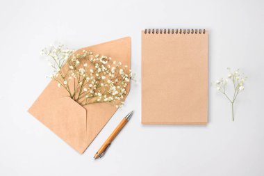 Güzel klasik düz kompozisyon, ahşap kalem, kraft kağıt defter ve kahverengi zarf, açık gri arka planda açık gri bebek nefesi çiçekleri, metin alanınız için kopya alanı.