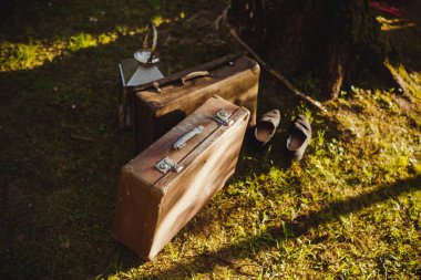 Yeşil çimlerin üzerinde eski kahverengi bavullar. Güneş ve ayakkabılar..